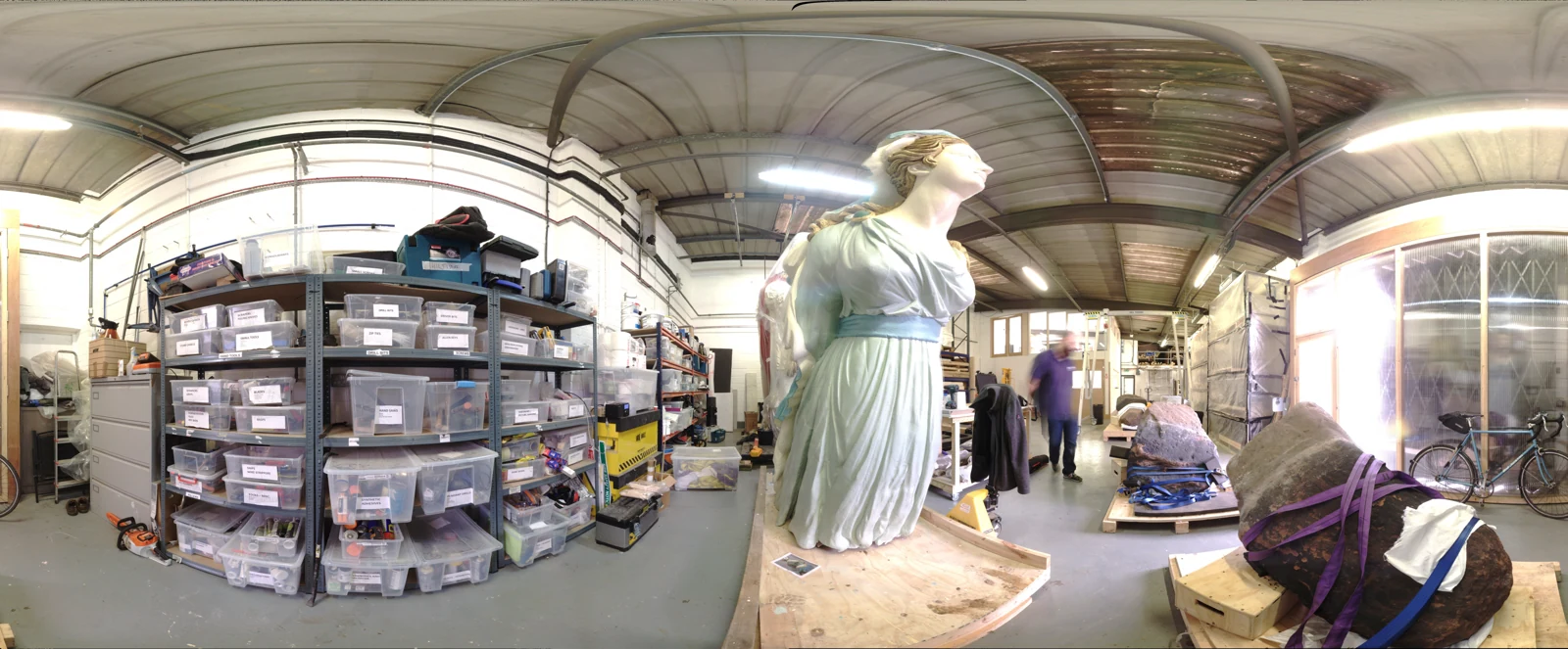 3D laser scanning panorama of a workshop storage space with shelving, crates, and a large statue on a pallet.