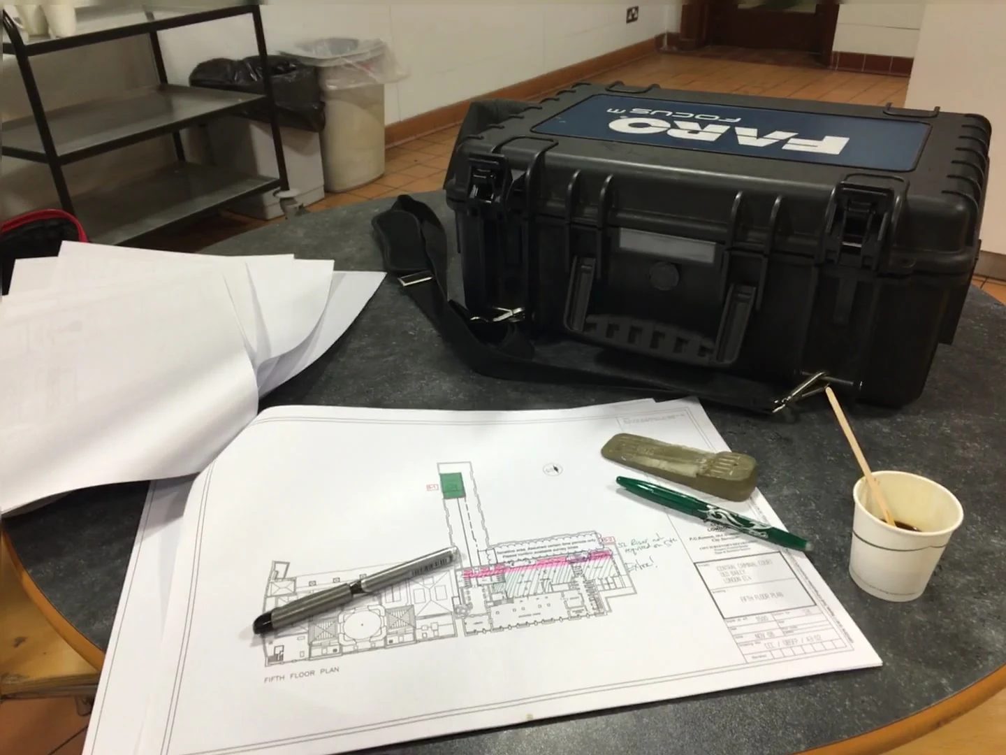3D laser scanning equipment case and floor plan drawings laid out on a table for survey planning.